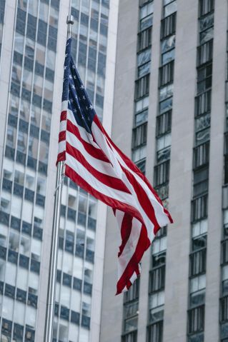 From below national US flag waving on pole against modern skyscraper in urban city district